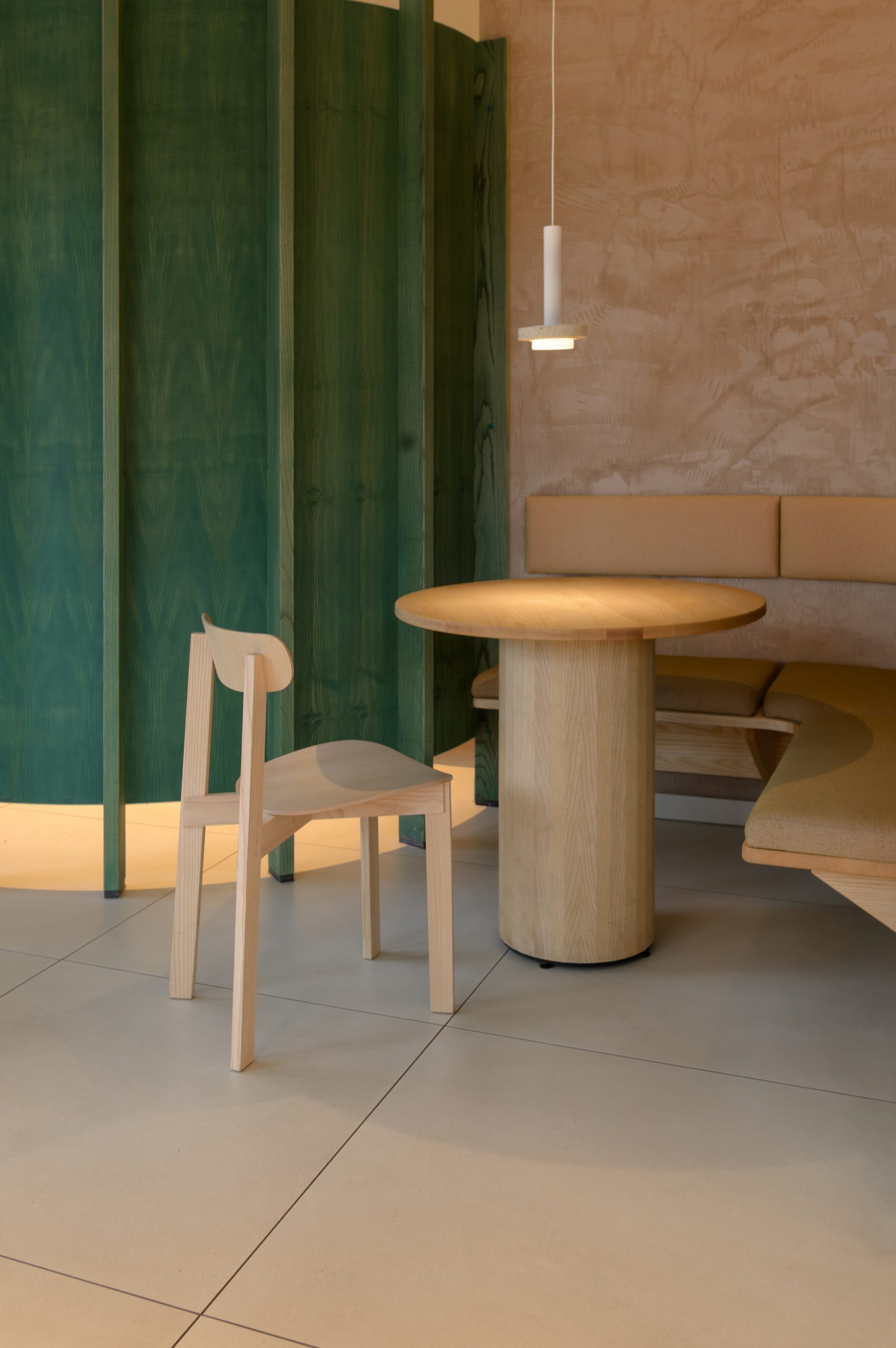 Sitzbereich bestehend aus Tisch und Stuhl. Im Hintergrund Raumtrenner aus grünem Holz